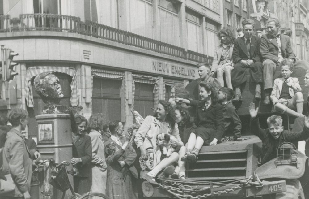 Feestvierende Amsterdammers zitten op een geallieerde pantserwagen.